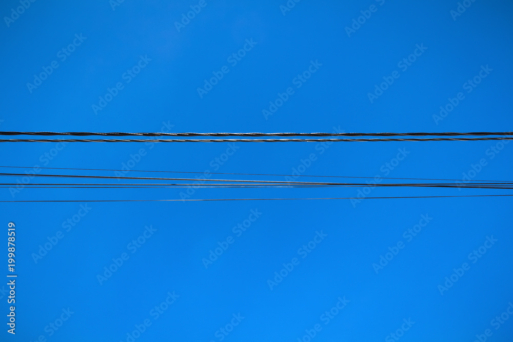 A line of electric wires close-up against a blue sky.