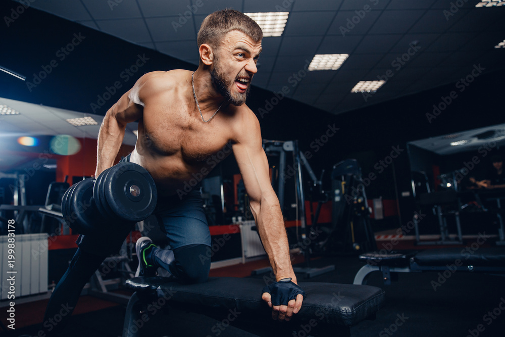 Man with muscles does an exercise with dumbbells on bench. Concept study of triceps, workout
