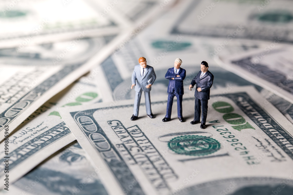 Miniature figurine toys standing on dollar with money and work concept. Focus on the businessman. Miniature figurine toys standing on dollar with money and work concept. Focus on the businessman.