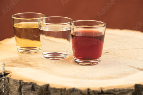 three glasses with different spirits are located on a wooden stump with annual rings, the texture of the cut is visible