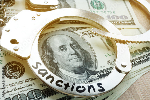 Word sanctions on a handcuffs and American dollar bills. Economical restrictive measures. photo