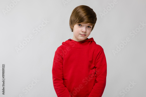 Cute confident little caucasian boy in red sweater on grey background