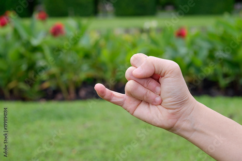 Woman hands showing little finger on green park background © feelartfeelant