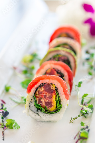 Fresh maguro maki sushi roll. A uramaki style sushi roll on a white plate. The raw sashimi tuna fish and rice are outside while nori is inside. This delicious meal is served in japanese restaurants.