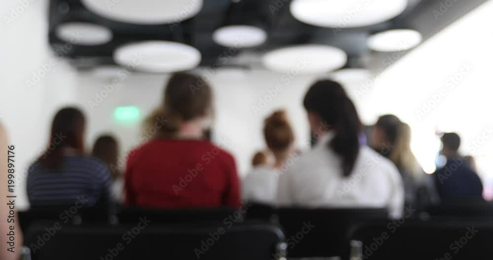 Women sit in class listening to a lecture at a conference back view. Blurred business people in meeting room.