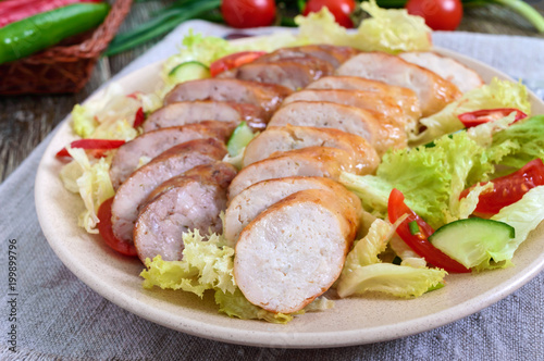 Juicy home made sausage with a light spring salad of fresh vegetables on a wooden table. A traditional Easter dish. Close up