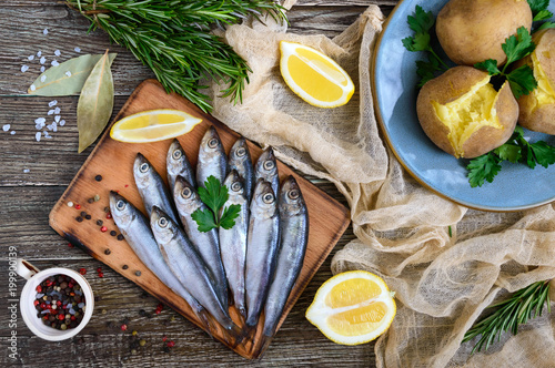 Canvastavla Boiled unpeeled potatoes in skins, a small salted fish of Baltic herring, sprats on a wooden table