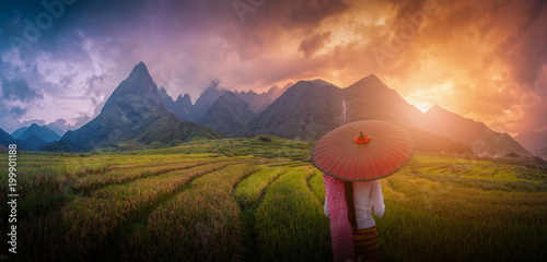 Woman holding traditional red umbrella on rice fields terraced at sunset in Sapa, Vietnam.