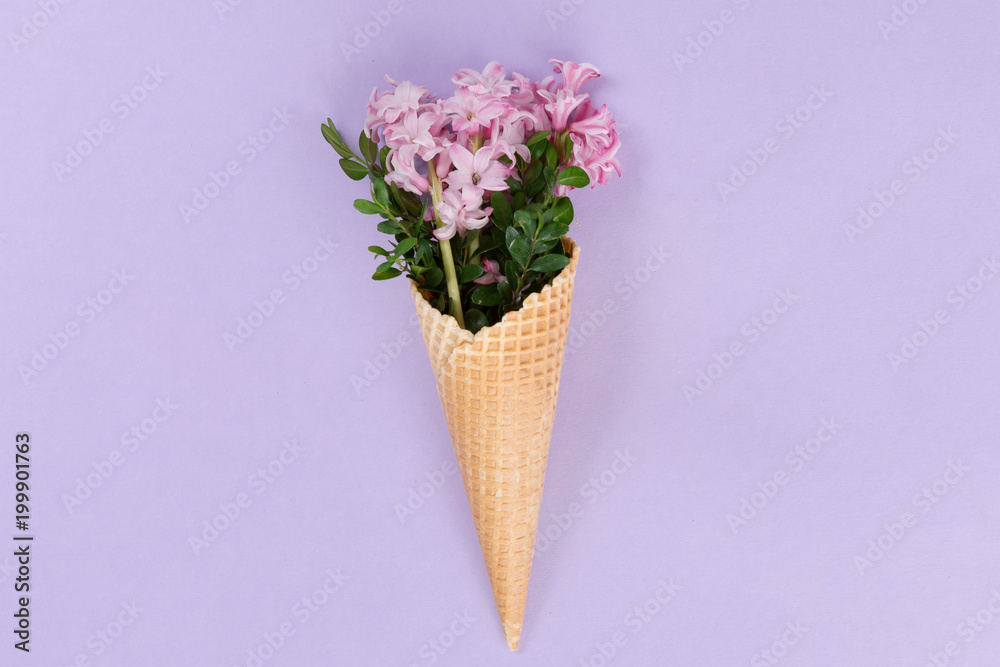 Top view of waffle cone with flowers bouquet on lilac or violet background, flat lay