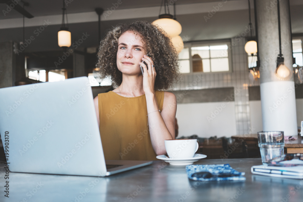 Portrait of woman talking on the mobile phone, sitting in the bright city cafe. Using laptop and working Portrait of woman talking on the mobile phone, sitting in the bright city cafe. Using laptop and working