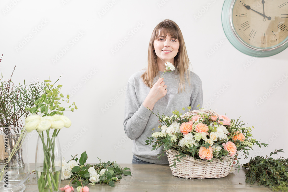 Smiling female florist. Floral workshop - woman making a beautiful flower composition a bouquet in a wicker basket. Floristry concept Smiling female florist. Floral workshop - woman making a beautiful flower composition a bouquet in a wicker basket. Floristry concept