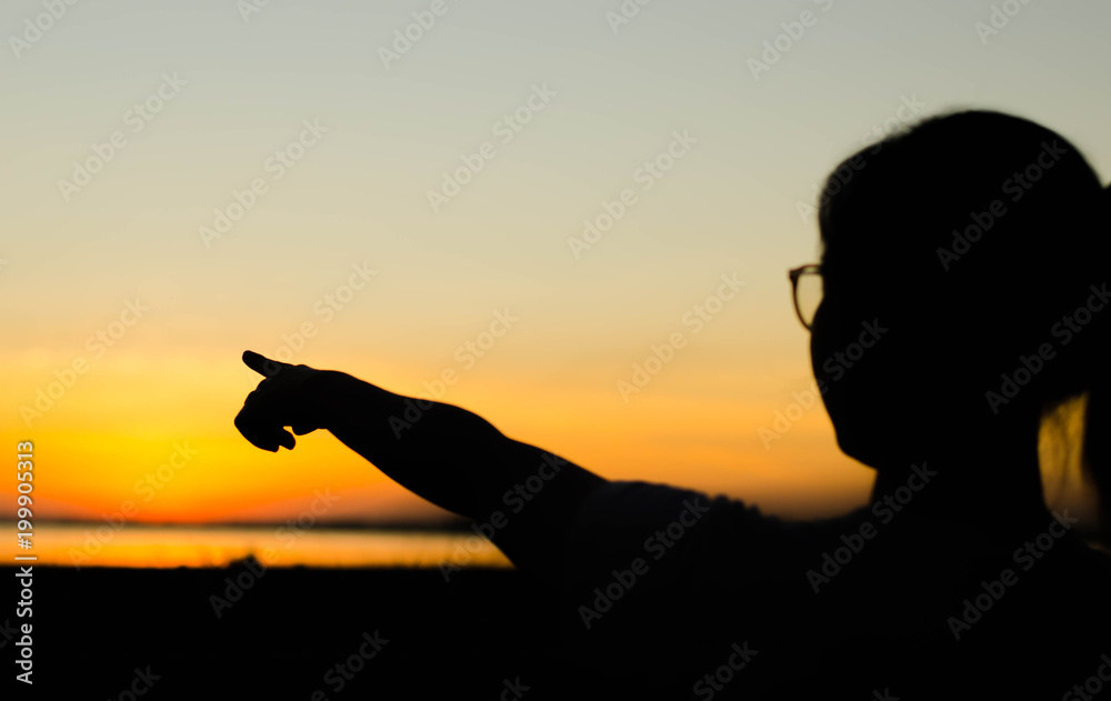 The silhouette of a woman standing pointing forward at sunset.