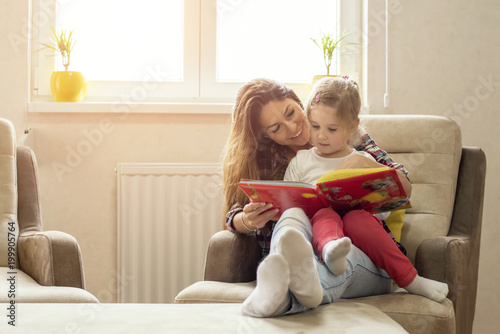 Mother and daughter reading book and having fun while spending time together at home