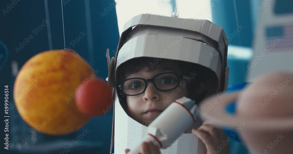CU Cute little boy wearing cardboard astronaut helmet flying toy rocket ...