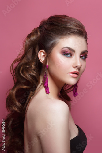 Fashion beauty portrait of a beautiful girl with a bright make-up and an elegant hairdress on a pink background.
