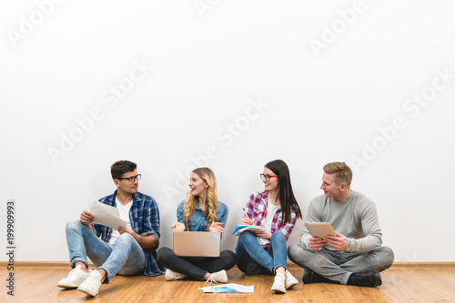 The four happy people sit on the floor on the white wall background