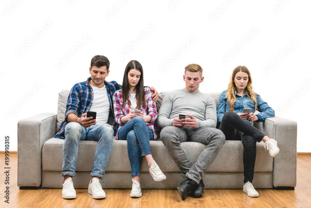 The four friends with phones sit on the sofa on a white wall background The four friends with phones sit on the sofa on a white wall background