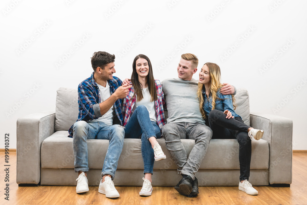 The four happy friends sit on the sofa on a white wall background