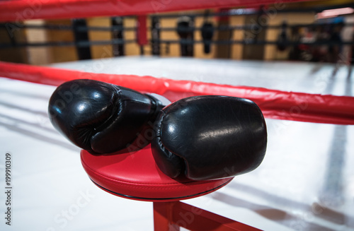 Black Boxing gloves are on the Boxing red chair. Boxing ring. Fitness room. © borislav15