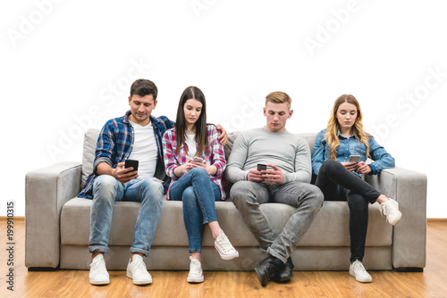 The four friends with phones sit on the sofa on a white wall background