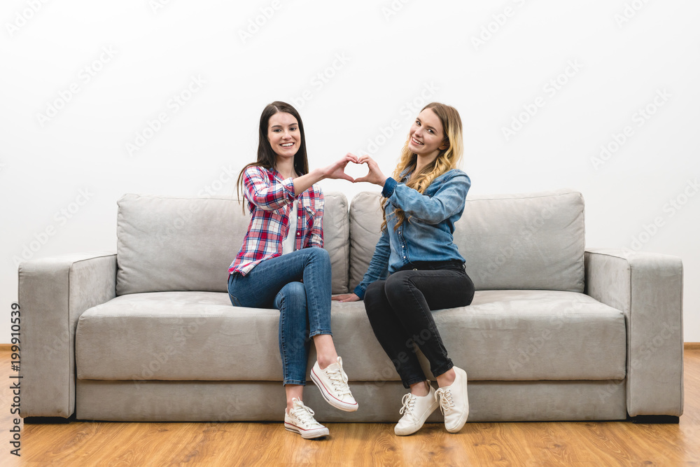 The two happy women show the heart symbol on the white wall background The two happy women show the heart symbol on the white wall background