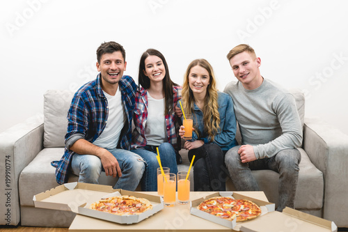 The happy friends with a pizza and drinks sit on the white background