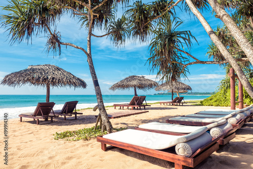 Beach beds with umbrellas on tropical beach, idyll and travel concept photo