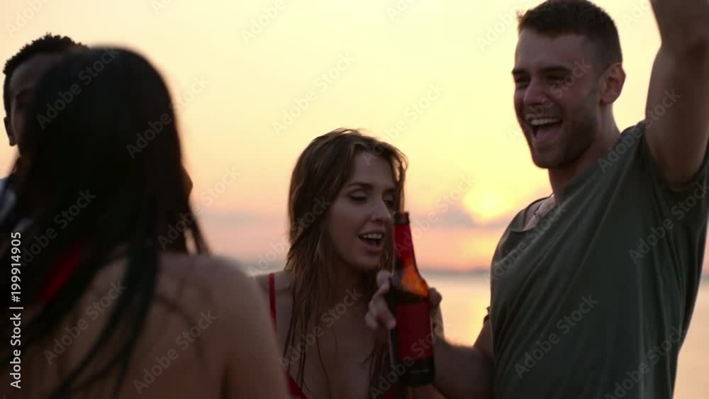Tilt up shot of happy friends drinking beer and dancing on beach at sunset Tilt up shot of happy friends drinking beer and dancing on beach at sunset