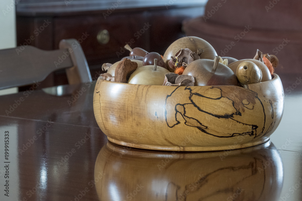 Hand turned wooden fruit bowl with hand turned wooden fruit sitting on and reflecting on ,reflection, a polished wooden table in a living room.