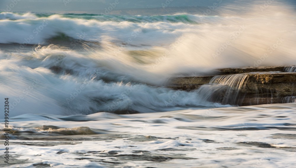Fototapeta premium Rocky seashore with wavy ocean and wind waves crashing on the rocks