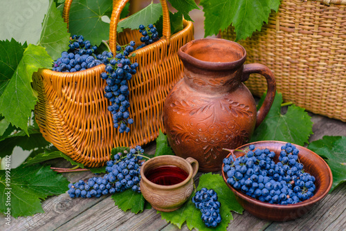 Baskets and bowl with grapes. Jar and cup with wine stand on on rustic wood. Wine making background. © Bohdan Petrushko