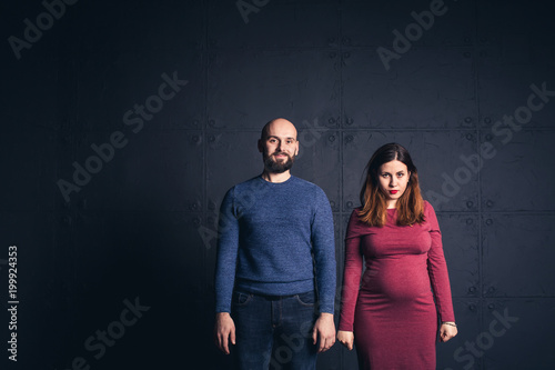 bearded man and pregnant woman looking in camera in studio on dark background. Copy space.