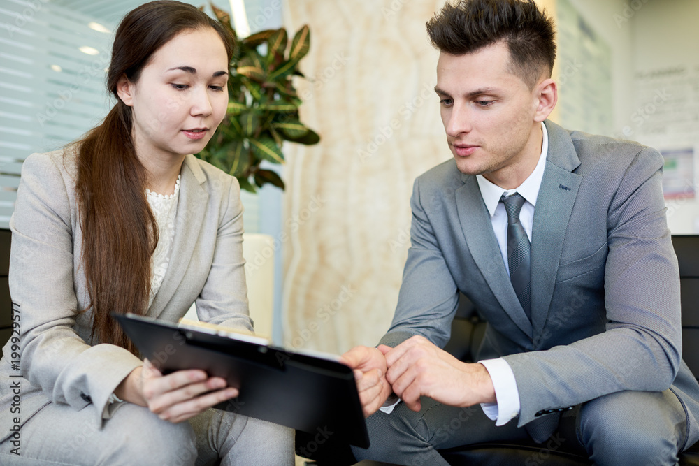 Portrait of successful young businessman and young woman during meeting sitting at coffee table in office Portrait of successful young businessman and young woman during meeting sitting at coffee table in office