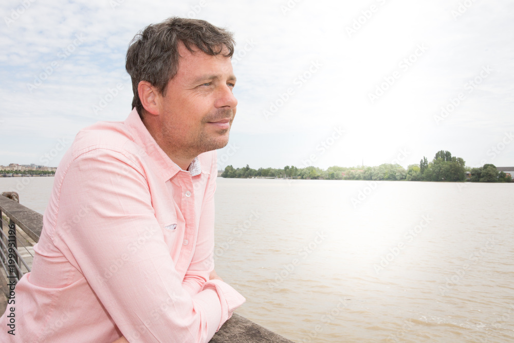 Thoughtful casual man outdoors looking up Garonne river and smiling in the Bordeaux city in France