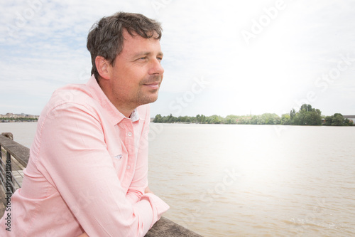 Thoughtful casual man outdoors looking up Garonne river and smiling in the Bordeaux city in France