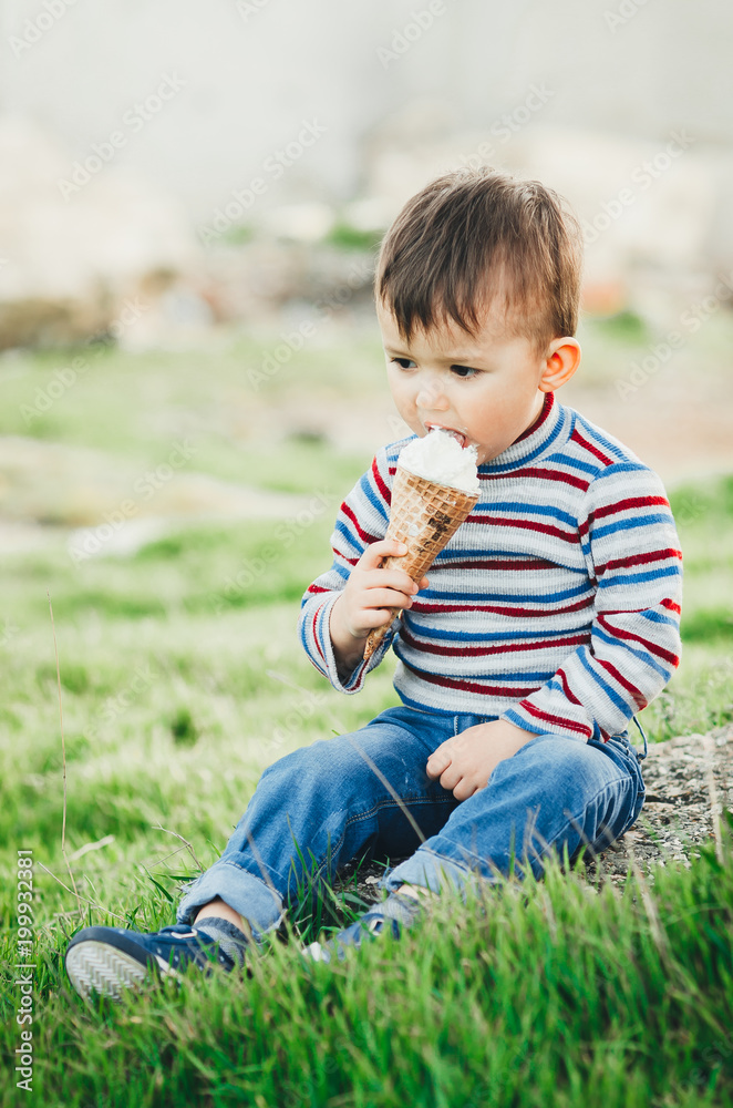 little cute boy eating ice cream three years very appetizing, amid nature, green grass little cute boy eating ice cream three years very appetizing, amid nature, green grass
