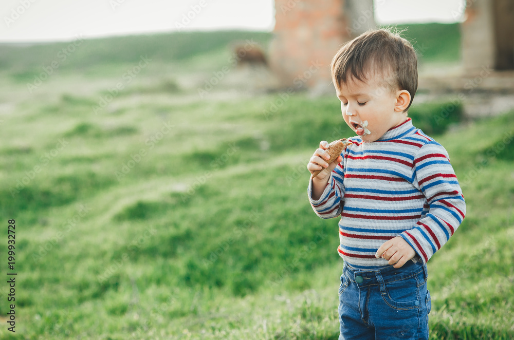 little cute boy eating ice cream three years very appetizing, amid nature, green grass little cute boy eating ice cream three years very appetizing, amid nature, green grass