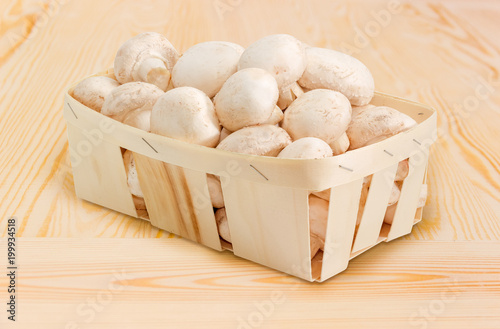 White button mushrooms in the wooden basket on wooden surface