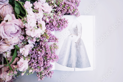 VORONEZH/RUSSIA-02.01.2018: Fashion book depicting old Dior dress with fresh flowers (roses, lilac and mattiolas in lavender color)on the light blue background photo