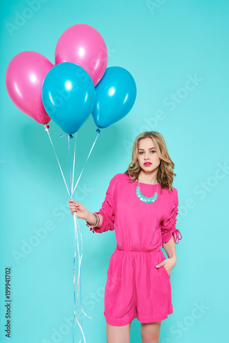 Gorgeous trendy young woman in party outfit holding bunch of balloons. Birthday Party concept on pastel blue background.