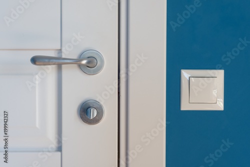 Close-up elements of the interior of the apartment. Detail of a white interior door with a chrome door handle and latch, light switch on the wall