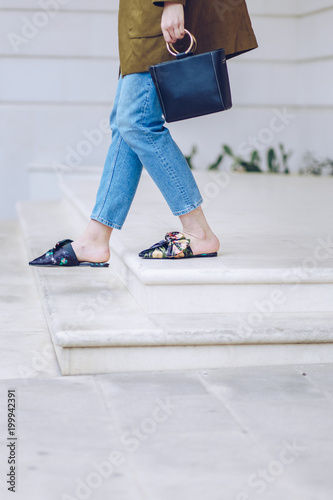spring/summer outfit fashion details, young stylish woman wearing denim jeans, black handbag and floral mules with a bow detail in front. urban fashion blogger posing outdoors, street style.