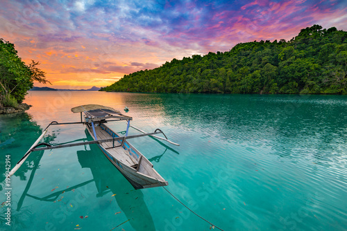 Togian Islands Indonesia sunset over caribbean sea, dramatic sky, traditional boat floating on blue green lagoon in the Togean Islands, Sulawesi, travel destination in Indonesia. photo