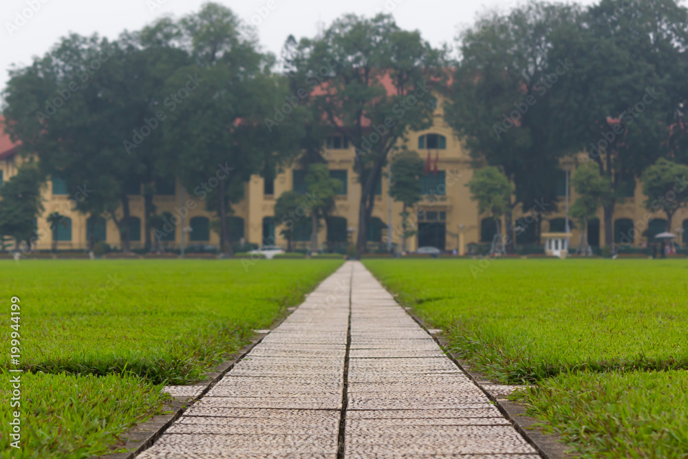 Concrete pathway and grass fields alongside with a yellow building in the background at Ba Dinh Square, Hanoi, Vietnam