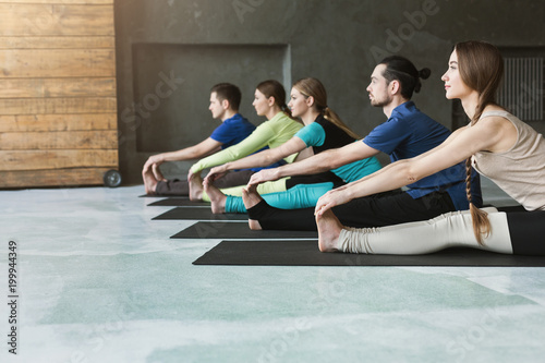 Young women and men in yoga class, doing stretching exercises
