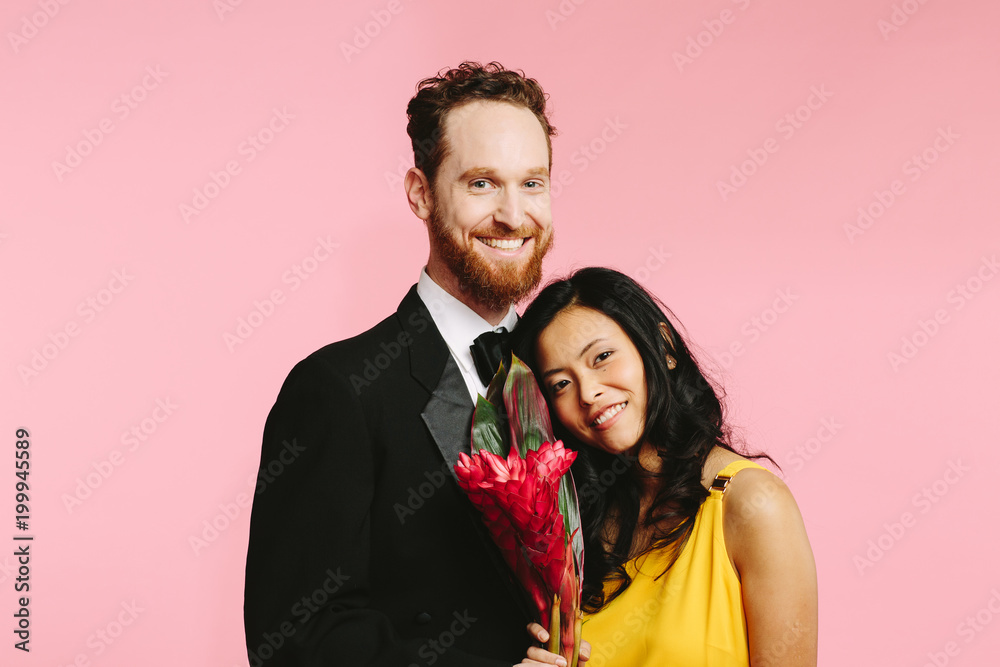 Portrait of an elegant couple, a caucasian man and asian woman, smiling and holding an exotic red flower Portrait of an elegant couple, a caucasian man and asian woman, smiling and holding an exotic red flower