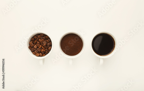 Roasted whole and ground coffee beans in cups, top view, white i