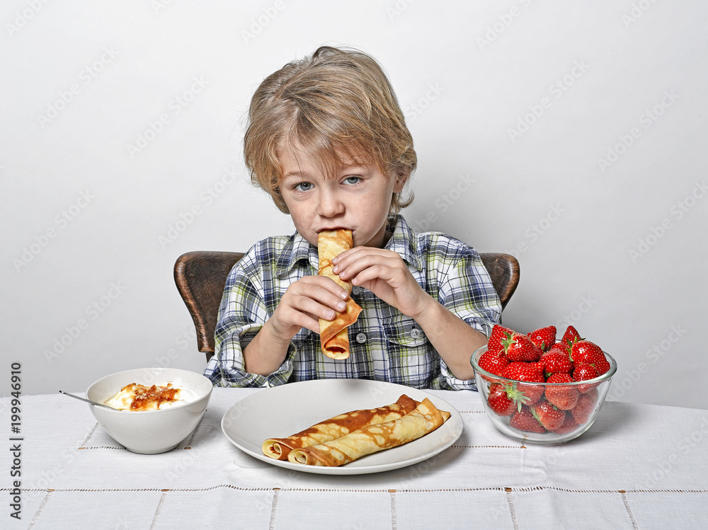 Boy at breakfast table eating pancakes and strawberries Boy at breakfast table eating pancakes and strawberries