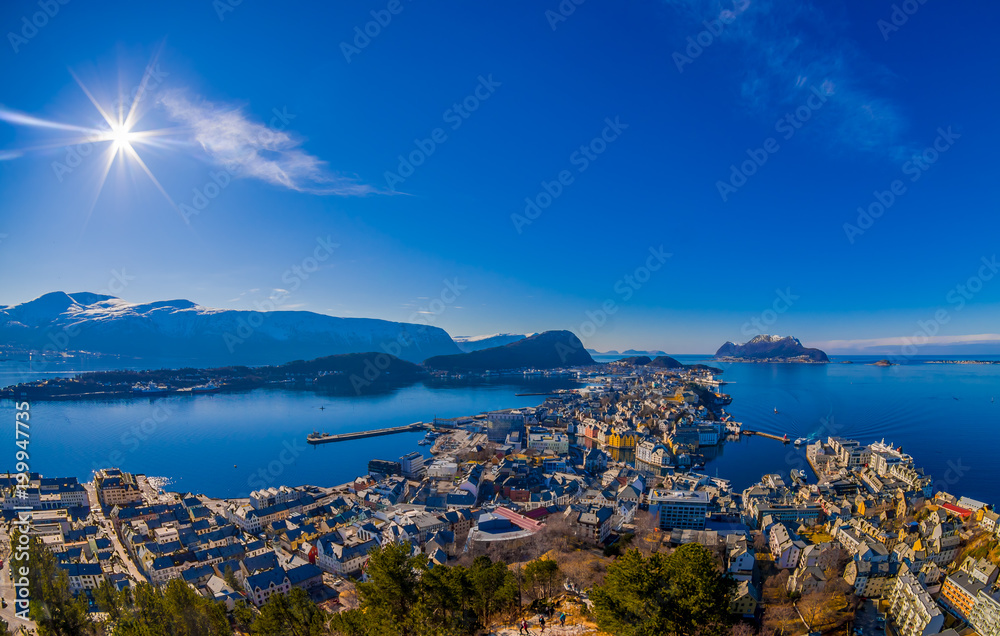 Amazing outdoor view of colorful buildings from the mountain Aksla at the city of Alesund with a huge mountain behind with sun shine at the blue sky
