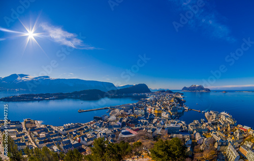Amazing outdoor view of colorful buildings from the mountain Aksla at the city of Alesund with a huge mountain behind with sun shine at the blue sky